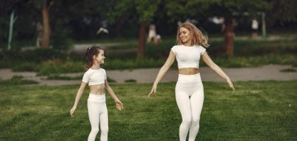 Mother and daughter bonding through outdoor exercise in activewear, featuring a joyful moment in a green park.